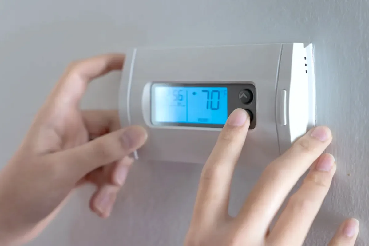 Hands adjusting a digital wall thermostat