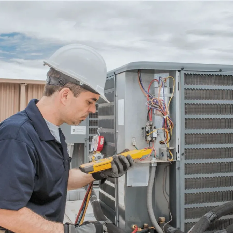 HVAC technician in a hard hat testing an outdoor air conditioner with a multimeter